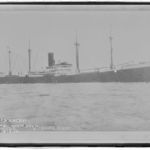 Schwarzweißfoto eines Frachtdampfers mit Mittelschornstein und drei Masten auf ruhigem Wasser; Museumswasserzeichen links unten.