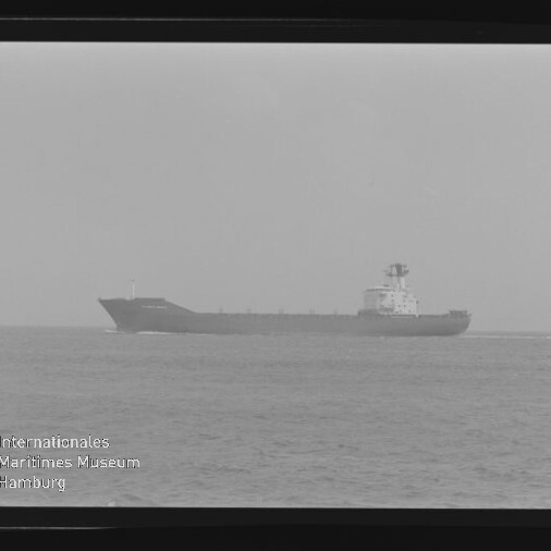 Schwarzweißfoto eines in Seitenansicht fahrenden Frachters auf ruhiger See, mit sichtbaren Negativrändern und dem Wasserzeichen „Internationales Maritimes Museum Hamburg“ unten links.