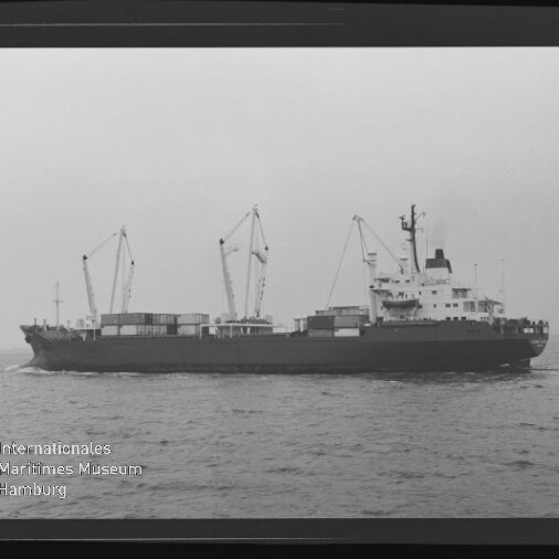 Schwarzweiß-Seitenaufnahme eines Frachtschiffs mit mehreren Ladekränen und Containern, das auf ruhiger See fährt; unten links das Signet ‚Internationales Maritimes Museum Hamburg‘.