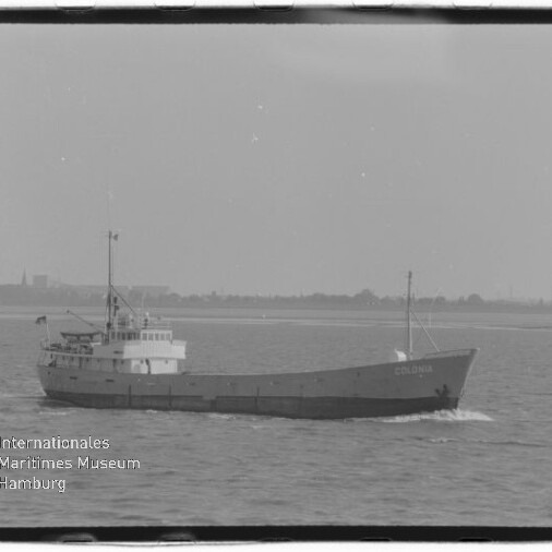Schwarzweiß-Foto eines Frachtschiffs mit dem Namen Colonia, das ruhig in Küstennähe fährt; im Vordergrund leicht welliges Meer und unten links das Logo sowie der Schriftzug des Internationalen Maritimen Museums Hamburg.
