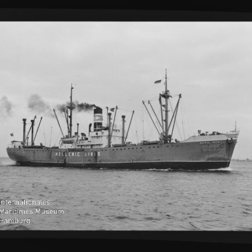Schwarzweißfoto eines Frachtschiffs der Hellenic Lines mit mehreren Ladebäumen und rauchendem Schornstein, das auf ruhiger See fährt; unten links ist ein Wasserzeichen des Internationalen Maritimen Museums Hamburg zu sehen.