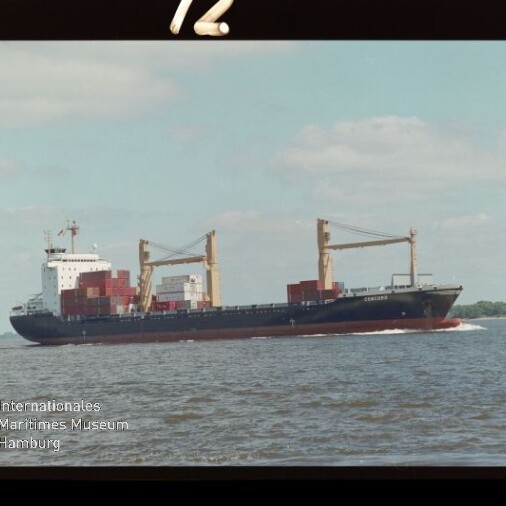 Containerfrachtschiff mit gestapelten Containern und zwei großen Ladekränen fährt auf ruhiger See unter hellem, leicht bewölktem Himmel; links unten Wasserzeichen des Internationalen Maritimen Museums Hamburg.