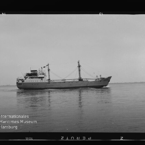 Schwarzweißaufnahme eines Frachtschiffs in Seitenansicht mit Ladebäumen und Aufbauten, das ruhig auf ruhiger See fährt; am unteren linken Rand das Logo des Internationalen Maritimen Museums Hamburg sowie Filmrand und -zahlen sichtbar.