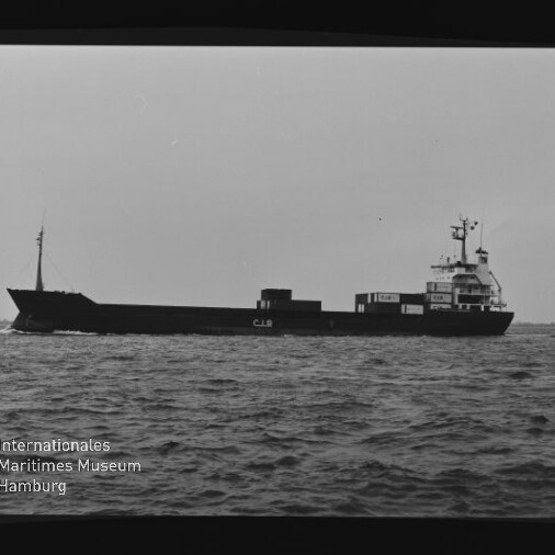 Schwarzweiß-Seitenansicht eines Frachtschiffs mit der Aufschrift CJS auf dem Rumpf und Containern am Heck, das auf leicht gewellter See fährt; links unten Wasserzeichen des Internationalen Maritimen Museums Hamburg.