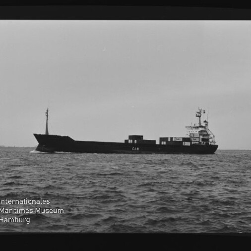 Schwarzweiß-Foto eines Frachtschiffs in Seitenansicht auf ruhiger See mit wenigen Containern an Deck; sichtbarer Filmrand und -nummern sowie links unten das Wasserzeichen des Internationalen Maritimen Museums Hamburg.