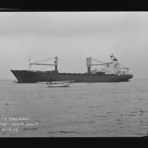 Großes Frachtschiff mit zwei Ladekranen fährt auf ruhiger See; im Vordergrund ein kleines Motorboot, links unten das Logo des Internationalen Maritimen Museums Hamburg und Filmrand mit der Zahl 13 sichtbar.