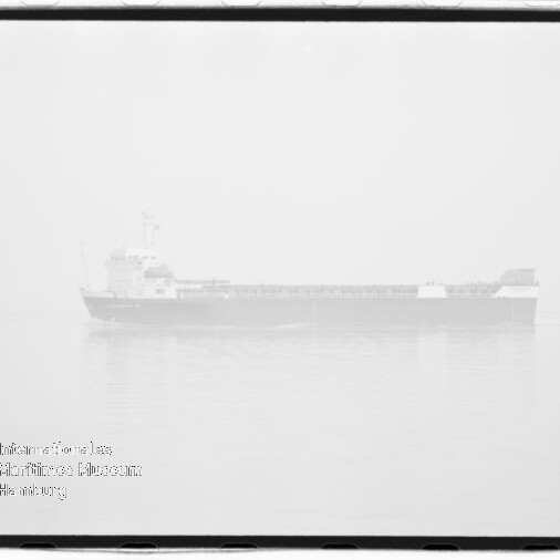 Schwarzweißaufnahme eines Frachtschiffs in dichtem Nebel über ruhigem Wasser mit schwacher Spiegelung, sichtbarem Wasserzeichen des Internationalen Maritimen Museums Hamburg unten links und Filmrand um das Bild.