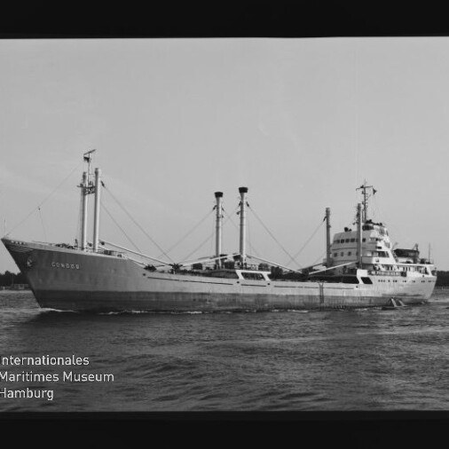 Schwarzweißaufnahme eines großen Frachtschiffs mit mehreren Masten und Ladebäumen, das auf ruhigem Wasser fährt; unten links ist das Logo des Internationalen Maritimen Museums Hamburg sichtbar.