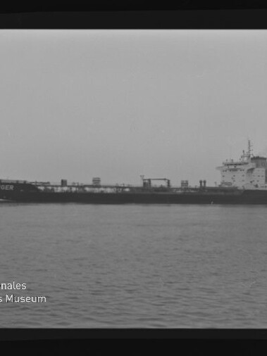 Schwarz-weiß-Fotografie eines langen Tankschiffs mit dem Namen CONGER an der Bordwand, das ruhig auf der See vor flachem Horizont fährt; im unteren linken Bildbereich das Logo und der Schriftzug des Internationalen Maritimen Museums Hamburg.