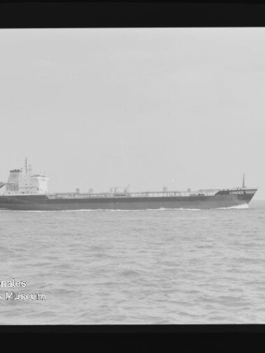 Schwarz-weiß-Foto eines Frachters, der von links nach rechts über eine ruhige See fährt; sichtbare Aufbauten am Heck, hoher Horizont, schwarzer Filmrand mit Markierung und Museumswasserzeichen unten links.