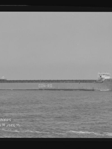Schwarzweißaufnahme eines langen Frachtschiffs mit der Aufschrift CON-RO am Rumpf, das seitlich auf ruhiger See fährt; Filmrand und Wasserzeichen des Internationalen Maritimen Museums Hamburg sind im Bild sichtbar.