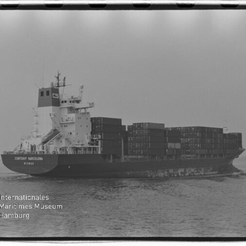 Schwarzweiß-Foto eines beladenen Containerfrachters auf ruhiger See, seitliche Ansicht mit aufgetürmten Containern und dem Logo des Internationalen Maritimen Museums Hamburg unten links.