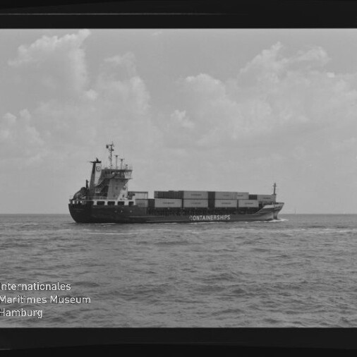 Schwarzweißaufnahme eines Containerschiffs mit gestapelten Transportcontainern, das auf ruhiger See unter bewölktem Himmel von links nach rechts fährt; Museumslogo „Internationales Maritimes Museum Hamburg“ unten links.
