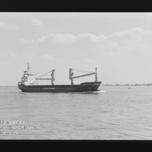 Schwarzweißaufnahme eines Frachtschiffs mit der Aufschrift CONTIMAR und zwei Ladekränen, das auf ruhiger See vor flachem Horizont mit vereinzelten Booten fährt; Filmnegativrand und Wasserzeichen des Internationalen Maritimen Museums Hamburg sichtbar.