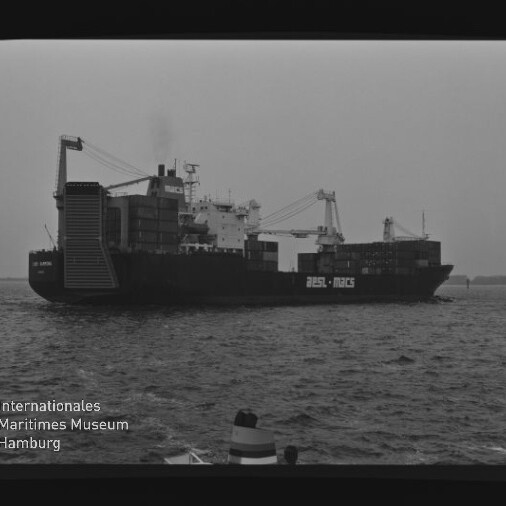 Schwarzweiß-Seitenansicht eines beladenen Containerschiffs mit Ladekränen und gestapelten Containern auf ruhiger See; Wasserzeichen des Internationalen Maritimen Museums Hamburg unten links.