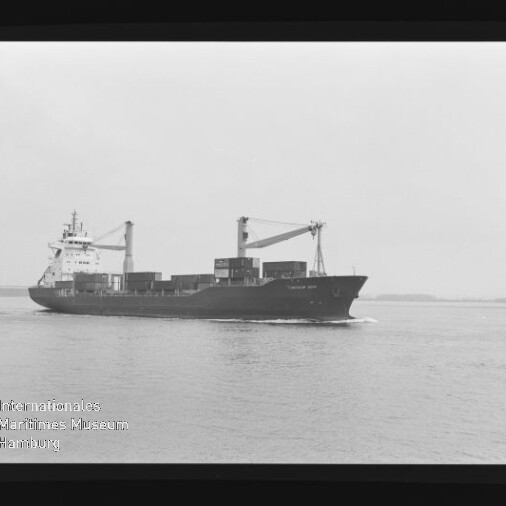 Containerschiff mit zwei Deckskranen und gestapelten Ladecontainern fährt ruhig auf dem Meer; unten links sichtbar das Logo des Internationalen Maritimen Museums Hamburg.