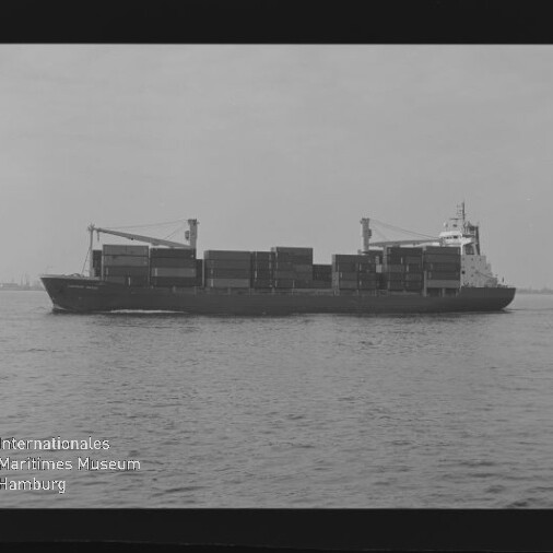 Schwarzweiß-Seitenansicht eines Containerschiffs mit gestapelten Containerblöcken und zwei Ladekränen, das auf ruhiger See vor flachem Horizont fährt; unten links sichtbar das Logo des Internationalen Maritimen Museums Hamburg.