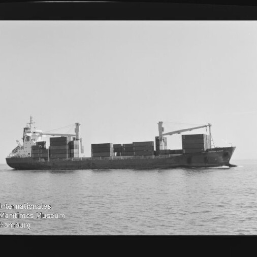 Schwarzweiß-Seitenansicht eines beladenen Containerschiffs mit aufgestapelten Containerblöcken und zwei Ladekränen an Deck, das ruhig auf dem Meer fährt; links unten sichtbar das Wasserzeichen des Internationalen Maritimen Museums Hamburg.