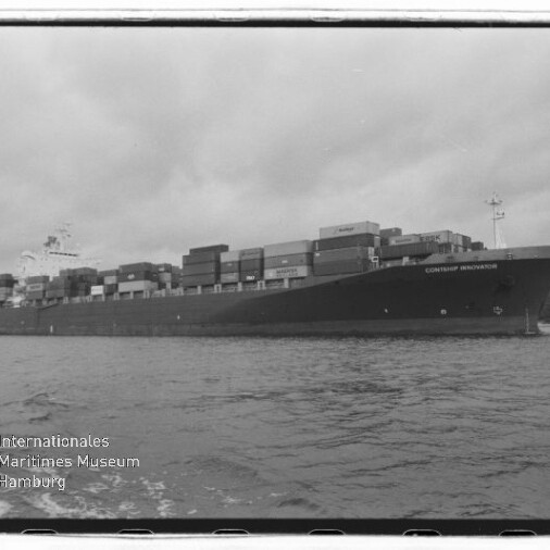 Großes Containerschiff mit zahlreichen aufgestapelten Frachtcontainern auf ruhigem Wasser unter einem bewölkten Himmel; links unten sichtbar das Wasserzeichen des Internationalen Maritimen Museums Hamburg.