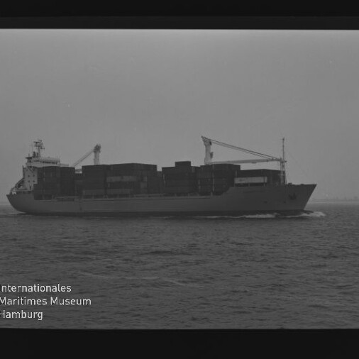 Schwarzweiß-Foto eines beladenen Containerschiffs mit aufgestapelten Containerreihen und zwei Ladekränen, das bei ruhiger See am Horizont entlangfährt; Filmrandmarkierungen und Wasserzeichen des Internationalen Maritimen Museums Hamburg sichtbar.