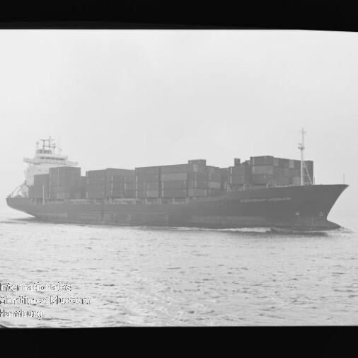 Schwarzweiß-Foto eines großen Containerschiffs auf offener See in seitlicher Ansicht, beladen mit gestapelten Containern; links unten ist ein Museumswasserzeichen sichtbar.