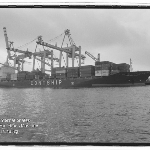 Schwarzweißaufnahme eines beladenen Containerschiffs mit dem Schriftzug CONTSHIP, das am Kai von mehreren Hafenkranen be- oder entladen wird; im Vordergrund Wasser und links unten das Logo des Internationalen Maritimen Museums Hamburg.