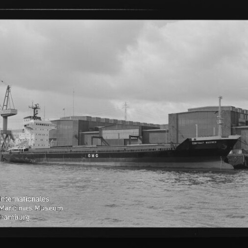Schwarzweißaufnahme eines am Kai liegenden Frachtschiffs mit der Aufschrift „CMC“, im Hintergrund Lagerhallen und ein Kran, im Vordergrund Wasser sowie sichtbarer Filmrand und Wasserzeichen des Internationalen Maritimen Museums Hamburg.