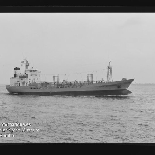 Schwarzweiß-Seitenaufnahme eines Frachttankers, der mit leichter Bugwelle auf offenem Meer fährt, sichtbar sind das Heckaufbauhaus, Masten und Tankdeckausrüstung; unten links das Wasserzeichen des Internationalen Maritimen Museums Hamburg.