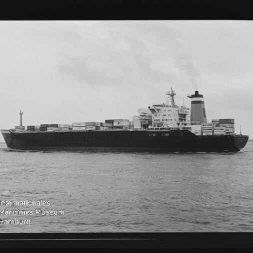 Schwarzweiß-Seitenansicht eines beladenen Containerschiffs auf ruhiger See mit gestapelten Containern, markanten Aufbauten und Schornstein, aufgenommen innerhalb eines sichtbaren Filmrahmens mit Filmmarkierungen und dem Logo des Internationalen Maritimen Museums Hamburg.