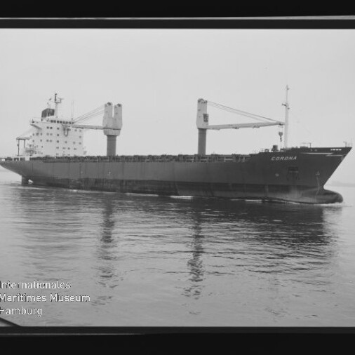 Großes Frachtschiff namens CORONA mit zwei markanten Deckskranen und achterlichem Aufbauten, ruhig auf spiegelglattem Wasser fotografiert, umgeben von sichtbarem Filmrand und Museumswasserzeichen unten links.