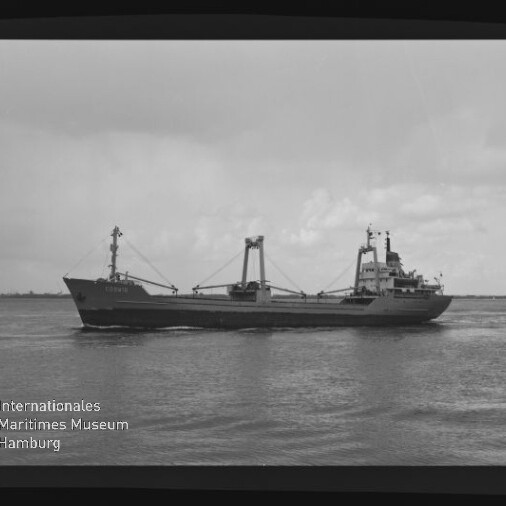 Schwarzweiß-Foto eines Frachtschiffs in Seitenansicht mit Ladekränen und Aufbau, das ruhig auf dem Meer vor niedrigem Horizont fährt; links unten Logo des Internationalen Maritimen Museums Hamburg.