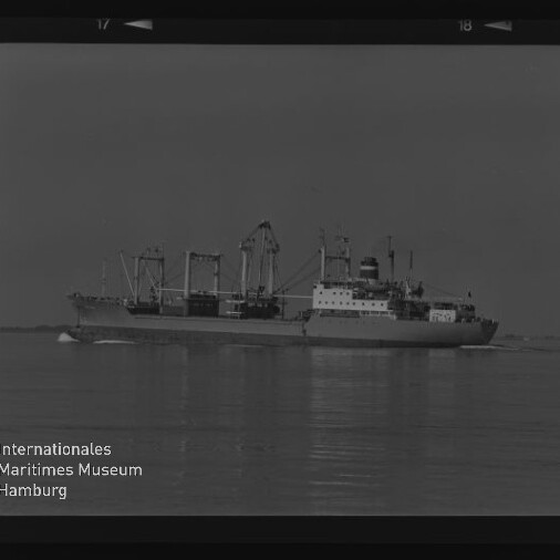 Schwarzweiß-Foto eines Frachtschiffs mit mehreren Ladekränen, das ruhig auf spiegelglattem Wasser fährt; unten links Logo und Schriftzug des Internationalen Maritimen Museums Hamburg.