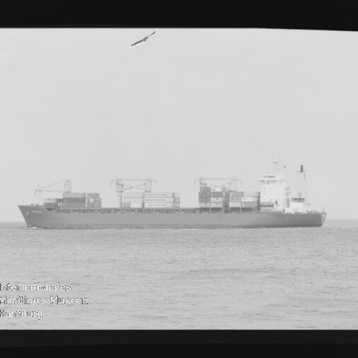 Graustufiges Foto eines Containerschiffs auf ruhiger See mit mehreren übereinander gestapelten Containern und Ladekränen, schwarzer Filmrand mit 'KODAK SAFETY'-Beschriftung und Wasserzeichen des Internationalen Maritimen Museums Hamburg unten links.