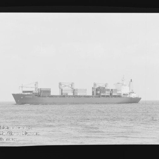 Seitenansicht eines Containerschiffs mit aufgestapelten Ladecontainern und mehreren Bordkränen auf ruhiger See vor hellem Himmel, links unten sichtbar das Wasserzeichen des Internationalen Maritimen Museums Hamburg.