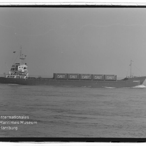 Schwarzweißaufnahme eines Frachtschiffs auf ruhiger See mit mehreren auf dem Deck gestapelten Containern, auf denen mehrfach „CAST“ steht, unten links Logo und Schriftzug des Internationalen Maritimen Museums Hamburg