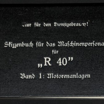 Schwarzer Buchumschlag mit weißer Frakturschrift: „Skizzenbuch für das Maschinenpersonal für ‚R 40‘ Band 1: Motorenanlagen“, oben rechts die Eintragung „Ausfertigung 5“ und links unten das Logo des Internationalen Maritimen Museums Hamburg.