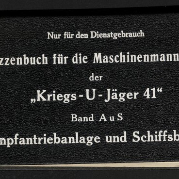 Schwarzer Leinenumschlag eines historischen Skizzenbuchs mit weißer Schrift: Titel ‚Skizzenbuch für die Maschinenmannschaft der „Kriegs‑U‑Jäger 41“ Band A u S — Dampfantriebsanlage und Schiffsbetrieb‘, runder handbeschrifteter Aufkleber links, Museumslogo unten links sowie kleine Aufschriften oben (‚Nur für den Dienstgebrauch‘, Ausfertigung 110).