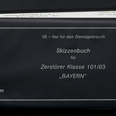 Schwarzes Skizzenbuch mit weißem Rahmen und aufgedrucktem Text VS – Nur für den Dienstgebrauch; Skizzenbuch für Zerstörer Klasse 101/03 „BAYERN“; links unten Museum-Logo und Schriftzug Internationales Maritimes Museum Hamburg; obere Kante zeigt eingeschobene Seiten.