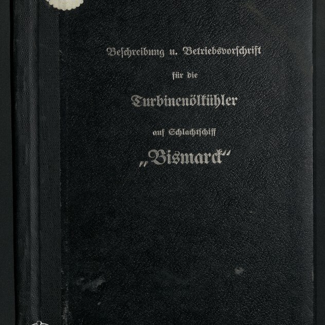 Schwarzer Leineneinband eines Handbuchs mit silberner Frakturschrift, auf dem als Titel die Betriebsanweisung für Turbinenöl mit dem Schiffsnamen „Bismarck“ steht; oben links ein runder Aufkleber, unten links das Logo des Internationalen Maritimen Museums Hamburg.