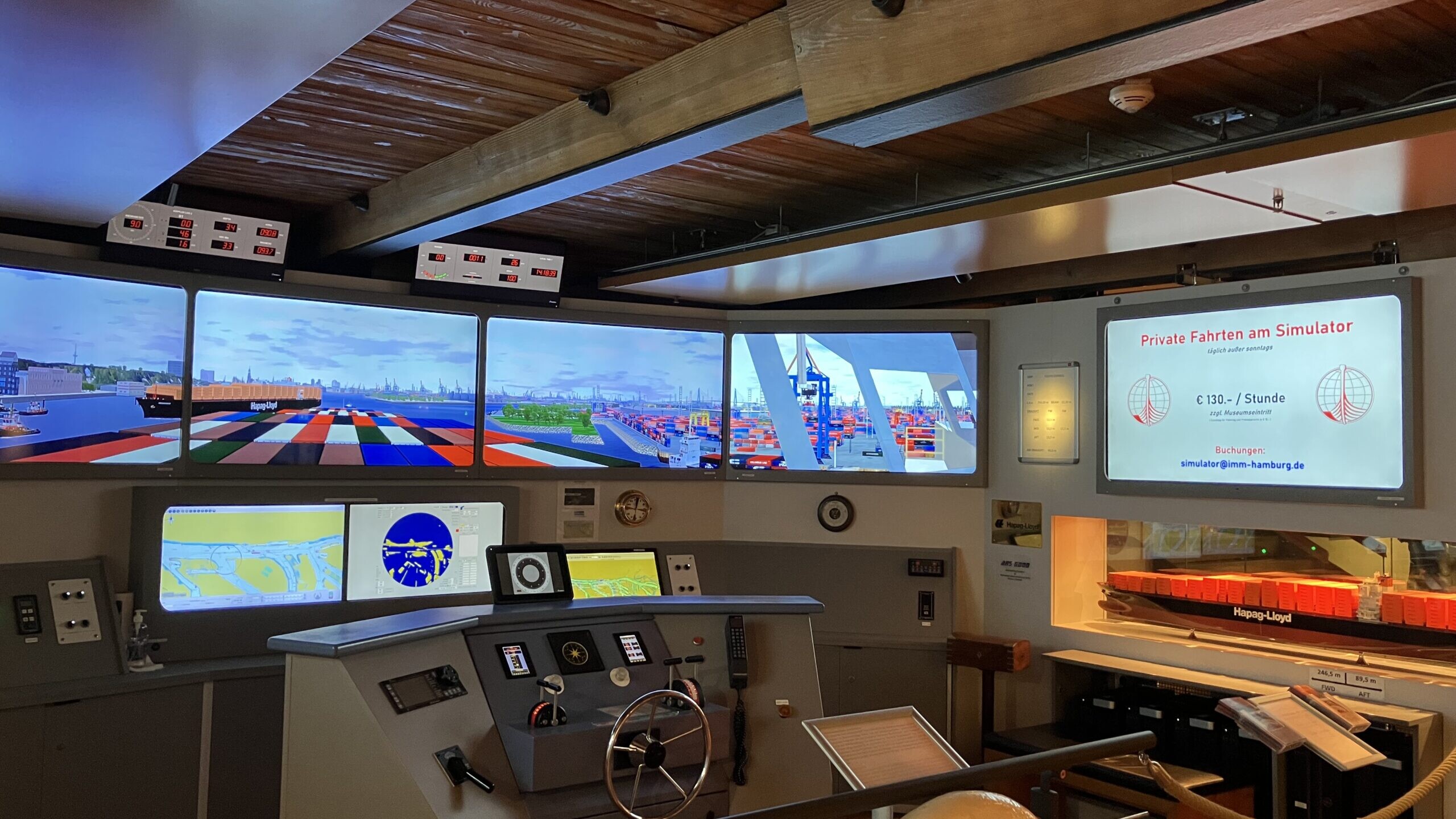 Schiffsbr&uuml;cken-Simulator mit Steuerrad, mehreren Bildschirmen mit Containerhafenansichten und Rettungsring 'PT EXPRESS'.