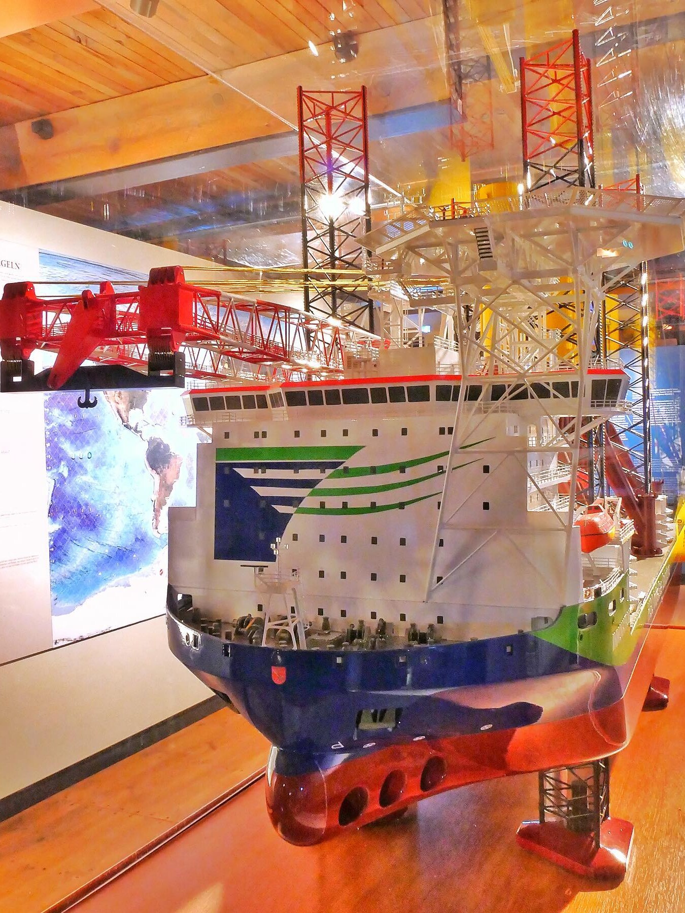 Modell eines großen Offshore-Schiffs mit rotem Kranarm, hellen Decksstrukturen und markanten Stützen im Ausstellungsraum