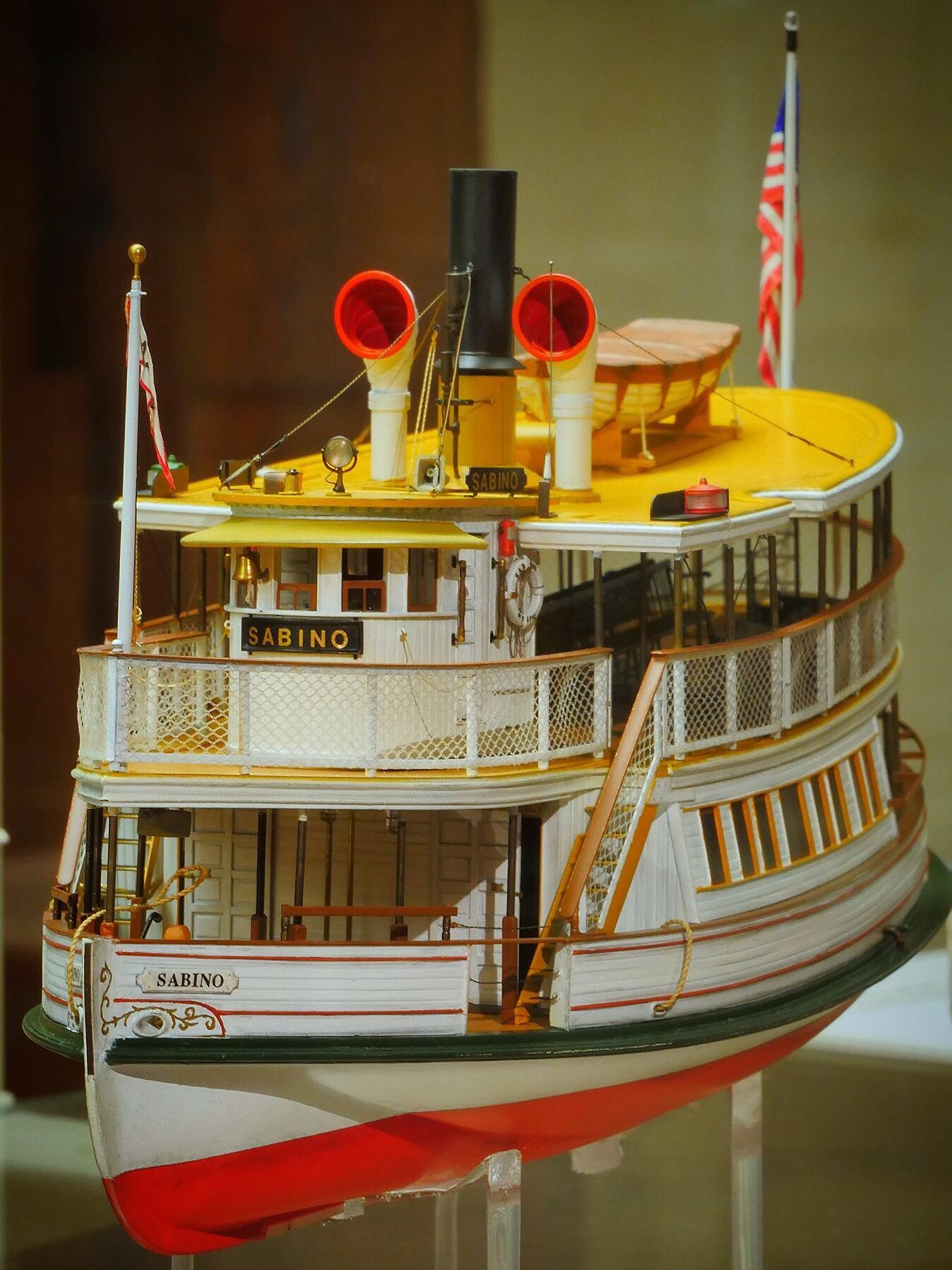 Detailliertes Modell eines weißen Raddampfers namens Sabino mit gelbem Oberdeck, Rauchrohr und amerikanischer Flagge.