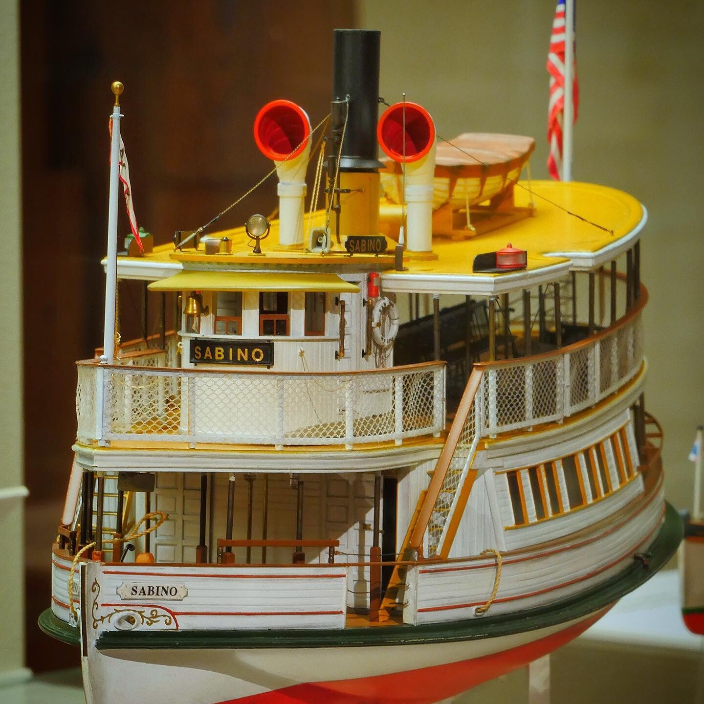 Detailliertes Modell eines weißen Raddampfers namens Sabino mit gelbem Oberdeck, Rauchrohr und amerikanischer Flagge.