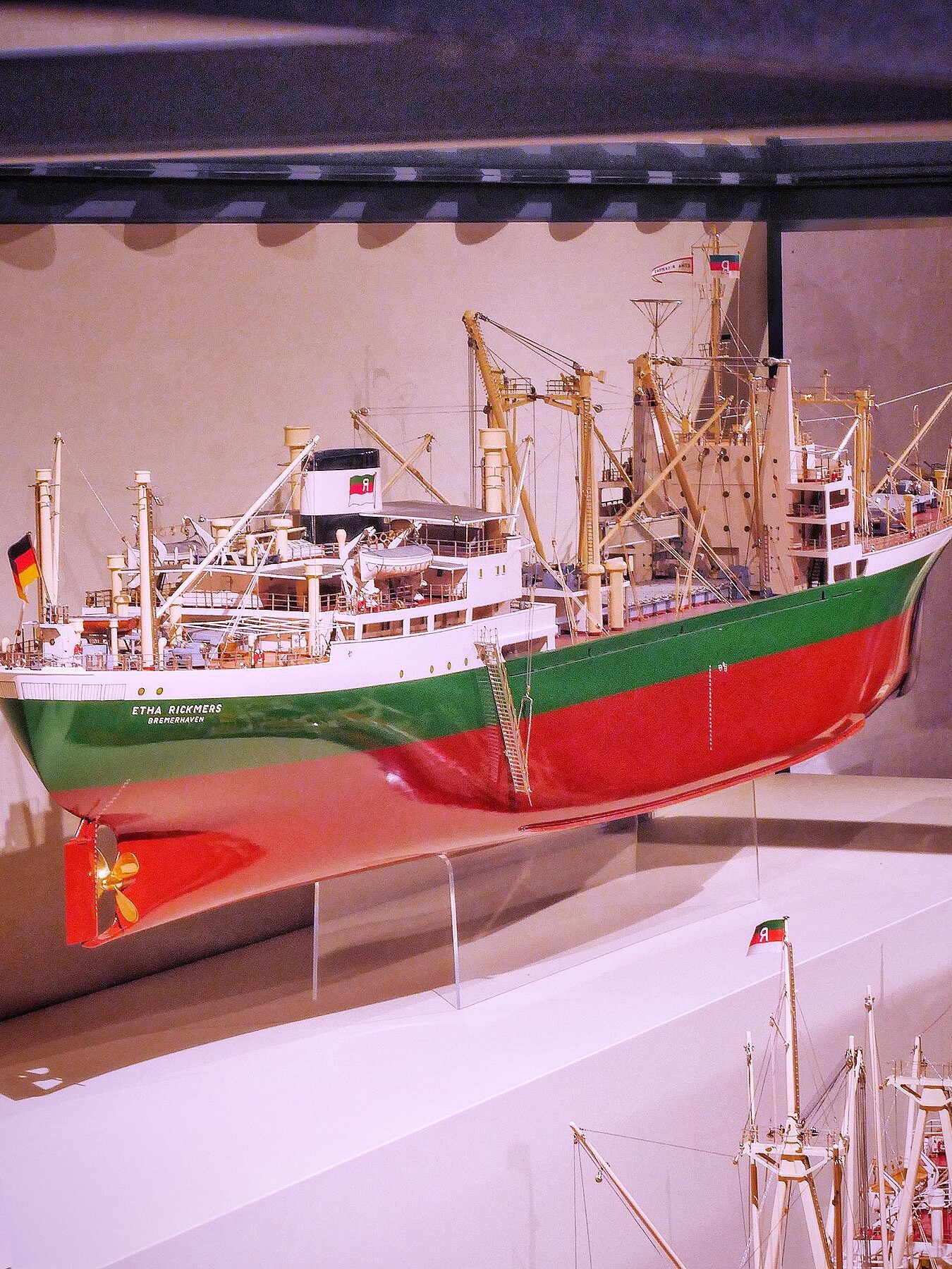 Modell eines großen Frachtschiffs mit grün-rotem Rumpf, zahlreichen Ladekränen und deutscher Flagge am Heck.