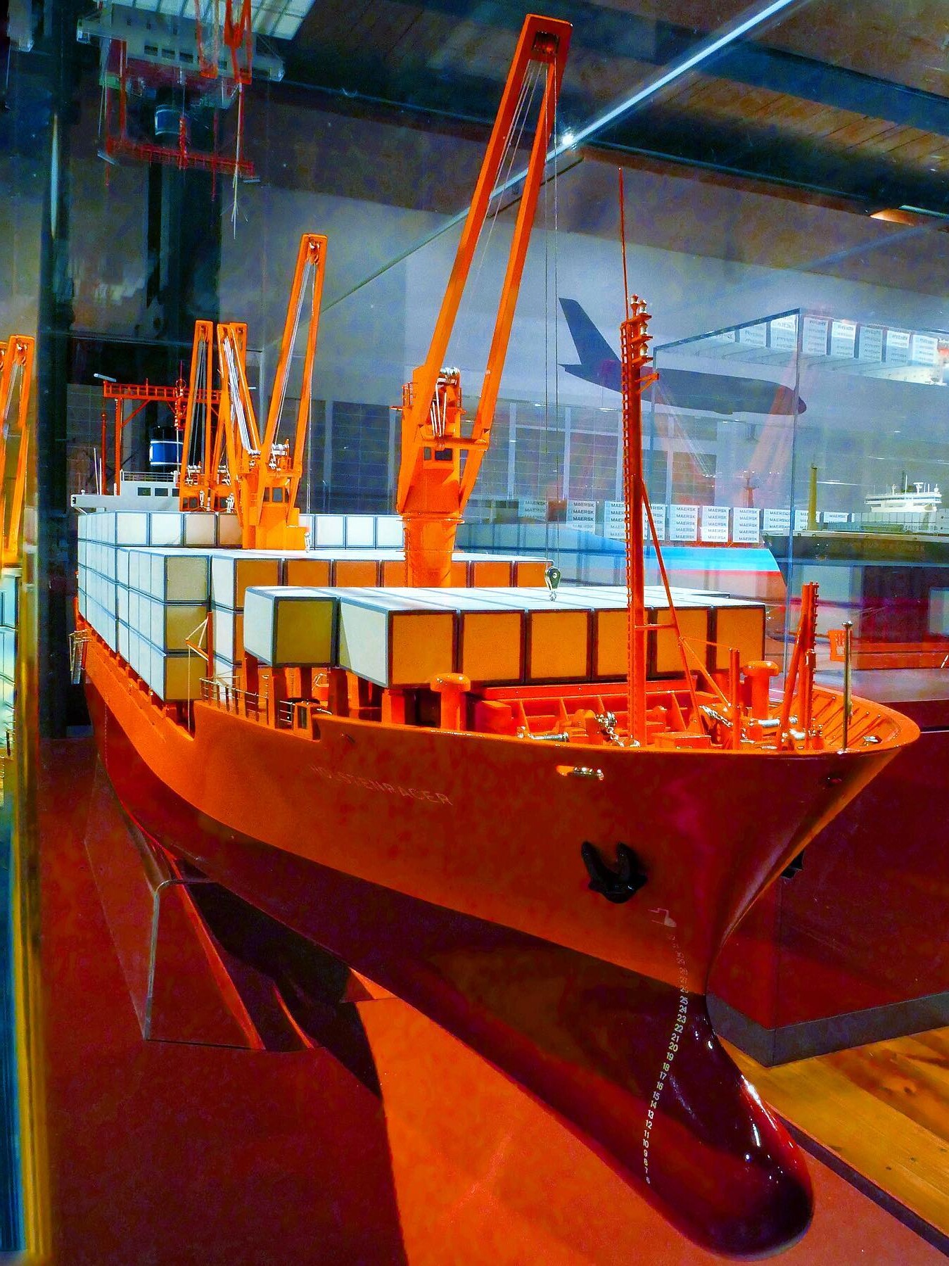 Rotes Containerschiff-Modell in Museumsvitrine mit aufgestapelten Containerblöcken und hohen Ladekränen.