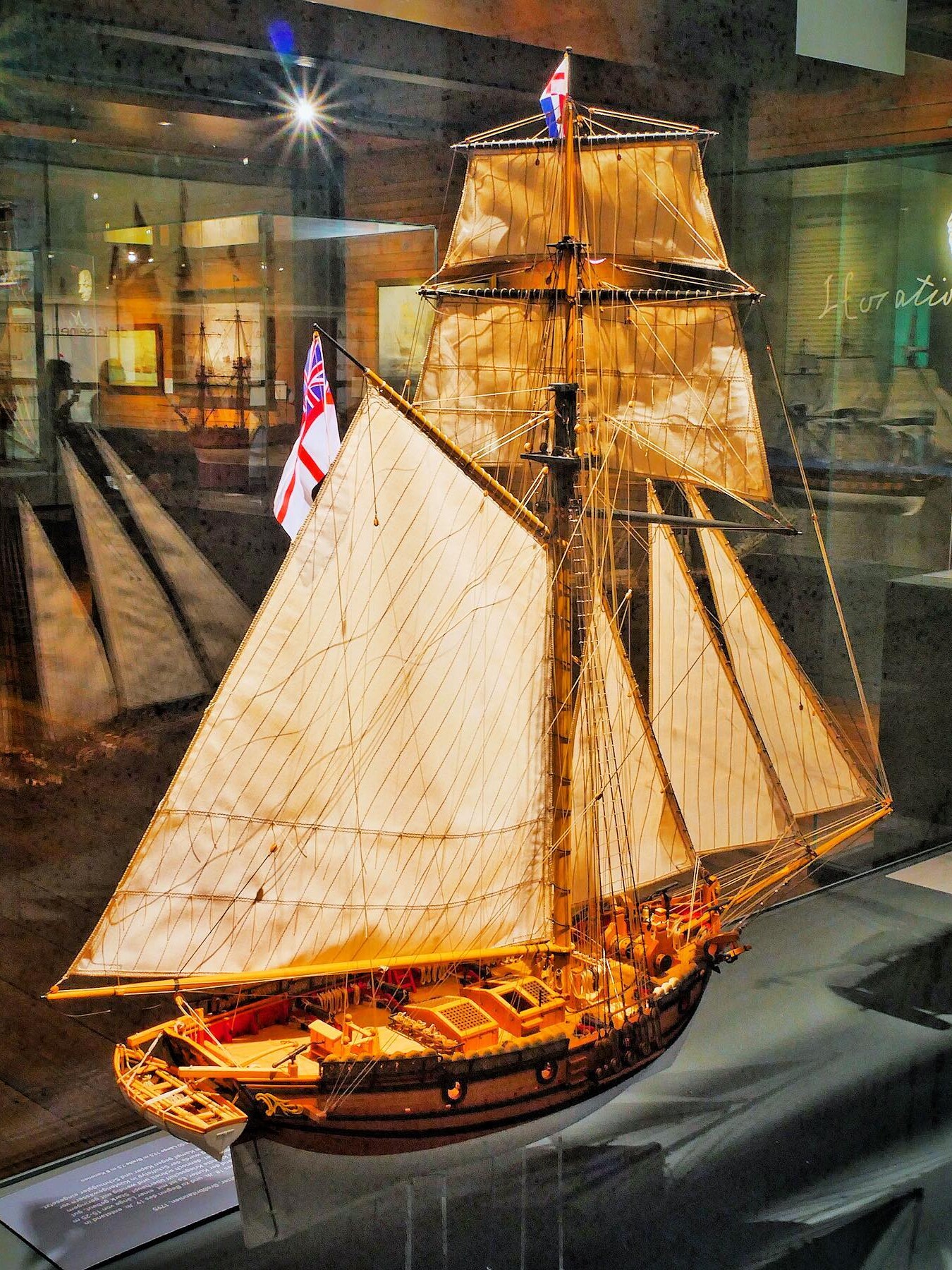 Holzmodell eines historischen Segelschiffs mit aufgeriggten Tuchsegeln, Takelage und britischer Flagge in Museumsvitrine.