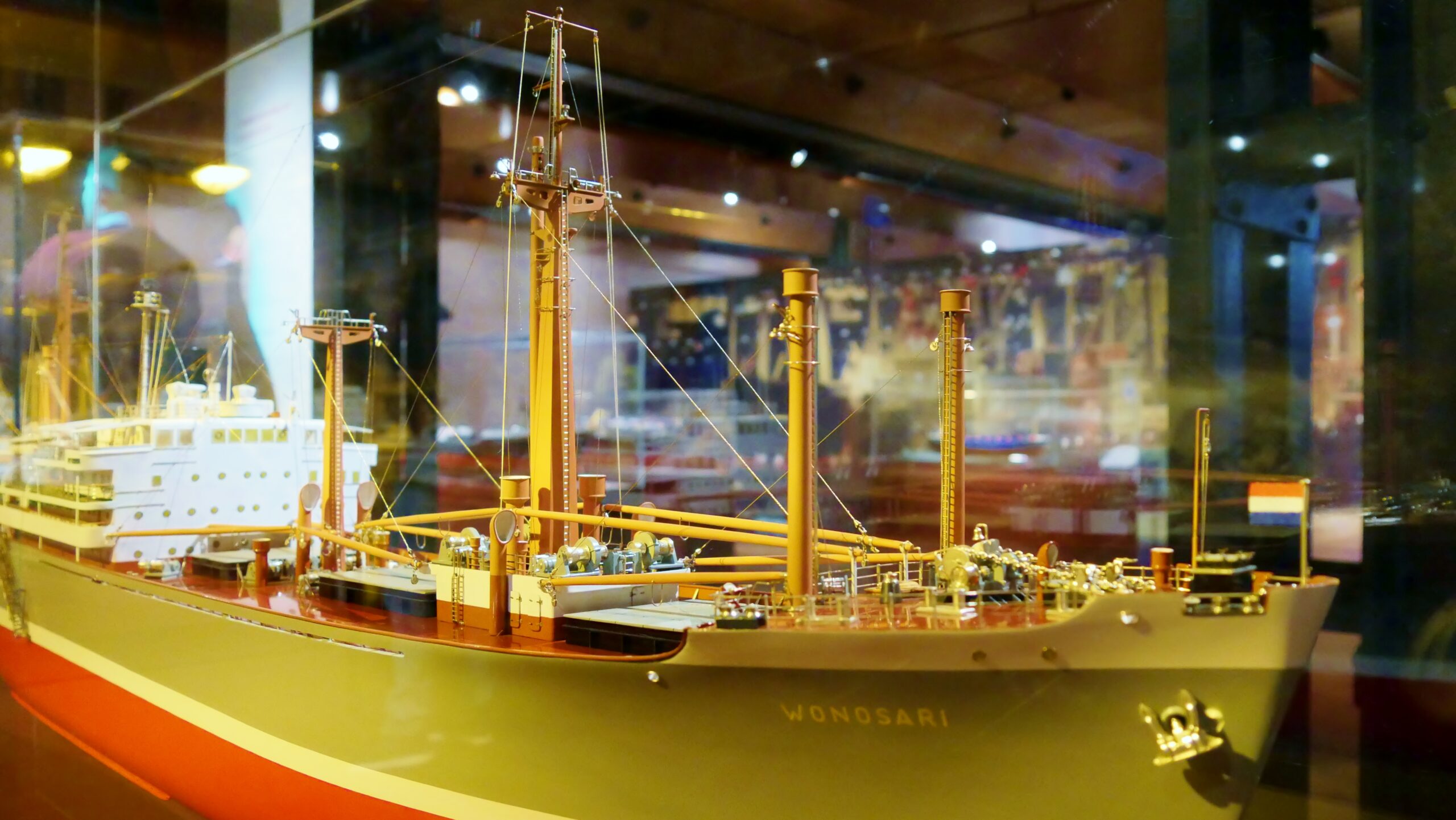 Detailliertes Schiffsmodell Wonosari mit Masten, Takelage und rotem Unterwasserschiff in einer beleuchteten Vitrine.