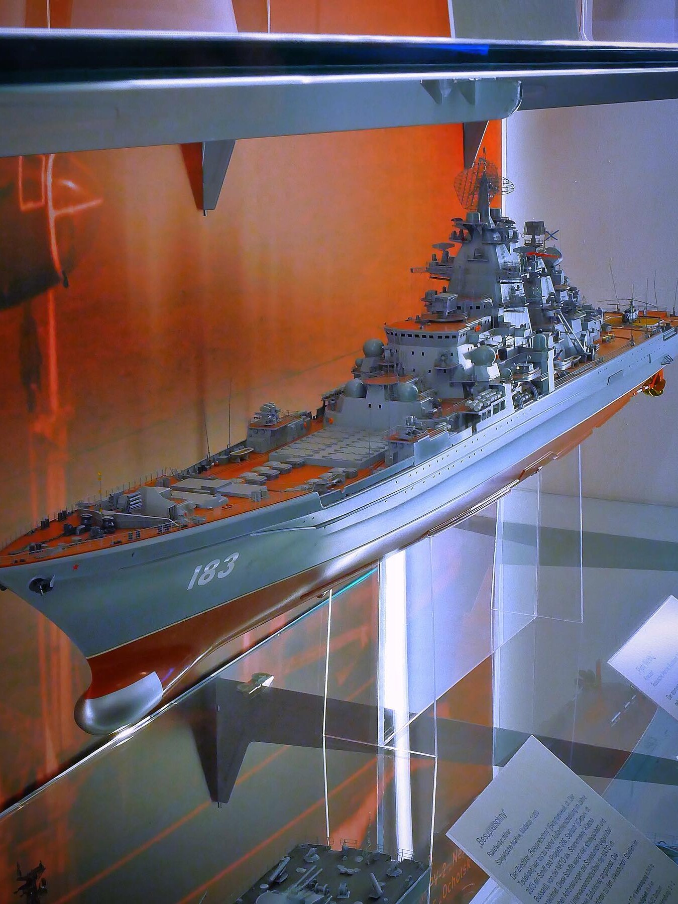 Detailliertes Modell eines grauen Kriegsschiffs mit der Nummer 183 auf dem Bug, auf Glasständern in einer Vitrine ausgestellt.