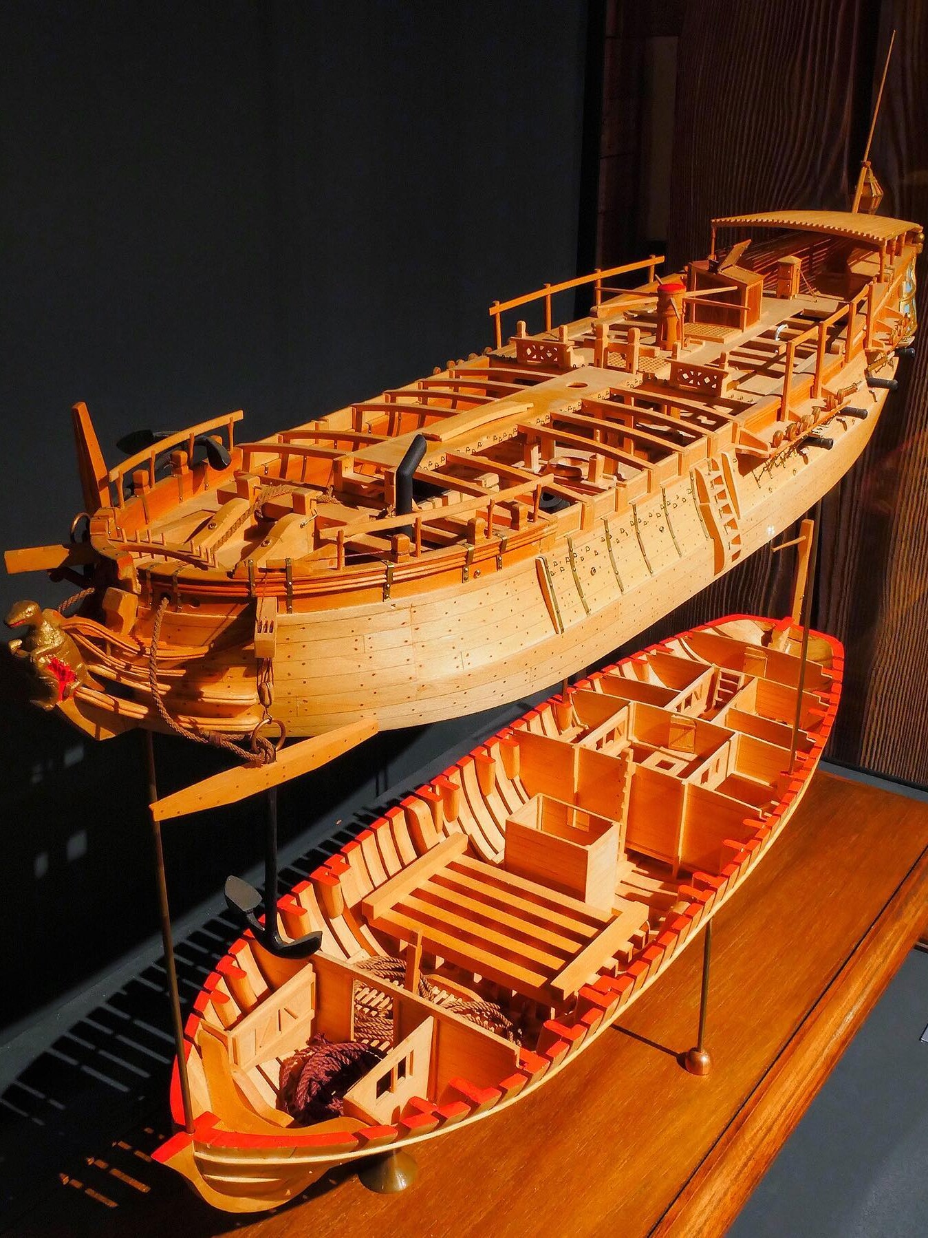 Zwei detaillierte hölzerne Schiffsmodelle nebeneinander, eines größer mit offenem Deck und Takelwerk, eines kleiner mit sichtbaren Spanten und roten Kanten.