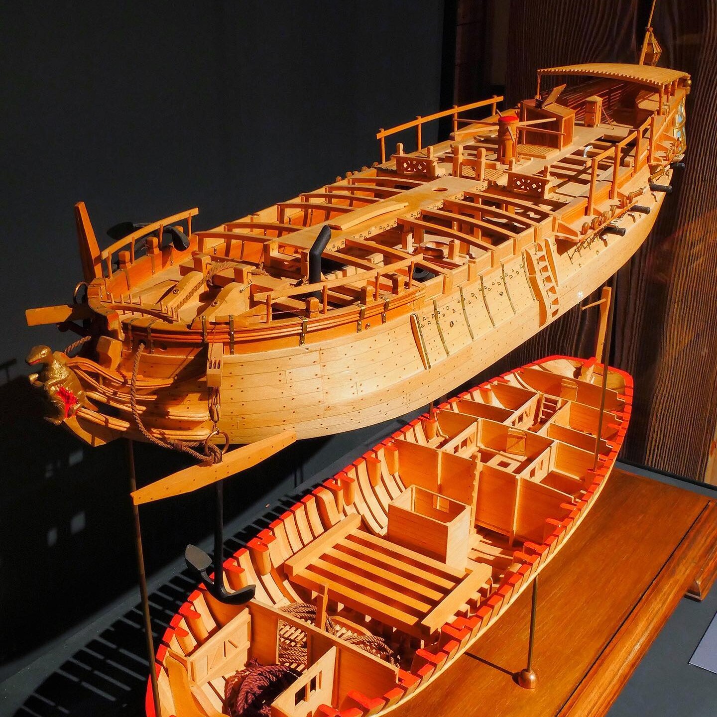 Zwei detaillierte hölzerne Schiffsmodelle nebeneinander, eines größer mit offenem Deck und Takelwerk, eines kleiner mit sichtbaren Spanten und roten Kanten.